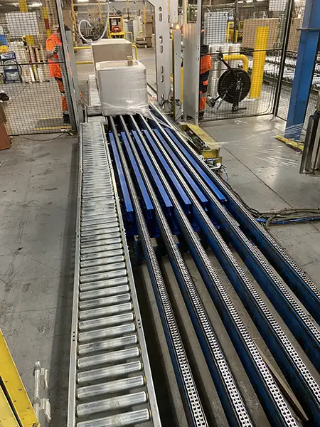 Module de réhausse de palettes intégré à un convoyeur à chaîne, fabriqué par TCM SAS pour une ligne de banderolage industrielle