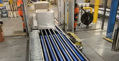 Module de réhausse de palettes intégré à un convoyeur à chaîne, fabriqué par TCM SAS pour une ligne de banderolage industrielle